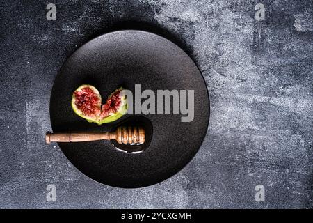 From above, organic honey drips from a wooden honey dipper on a sleek black plate, neatly complemented by a sliced fig. Perfect for representing natur Stock Photo