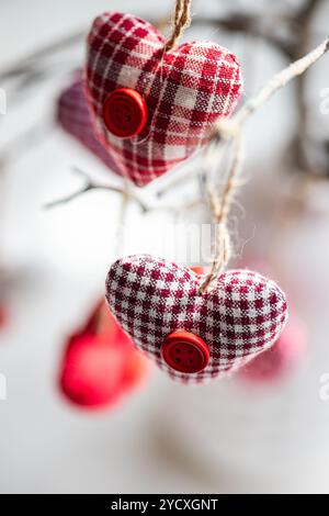 A close-up photo showcasing fabric hearts with a tartan pattern and red buttons, hanging on twist ropes, adding a romantic vibe to a table setting Stock Photo