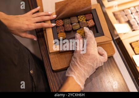 A customer selects from a variety of artisanal chocolates displayed in a wooden storage box, focusing on an individual piece Stock Photo