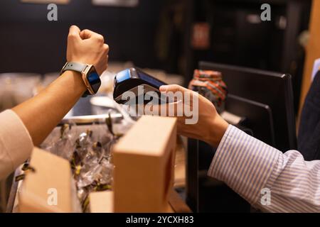 Customer making a contactless payment using a smartwatch at a chocolate store checkout, adding convenience and modernity to the shopping experience Stock Photo