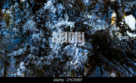 Intricate details of bubbling water over dark rocks, capturing the contrast and movement in a natural aquatic setting. Stock Photo