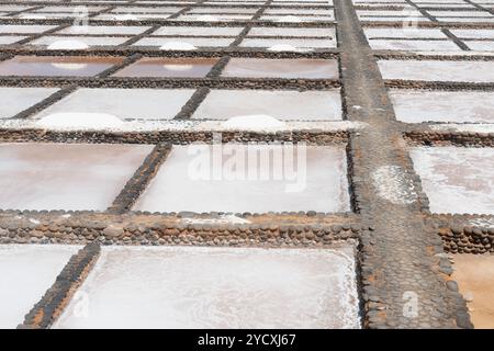An aerial view of organized salt pans, showcasing various stages of sea salt crystallization, with pathways delineated by pebbles Stock Photo
