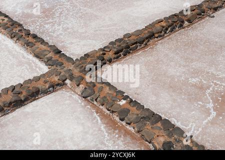 Detailed view of salt crystallization in a traditional salt pan, showcasing the intersection of mud walls lined with black volcanic stones Stock Photo
