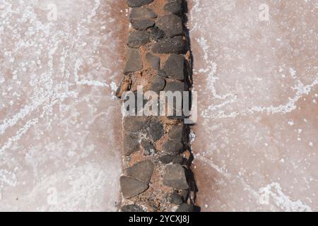 Close-up view of white salt crystals naturally forming on a crumbling stone barrier within a saltpan, reflecting the traditional methods of salt produ Stock Photo