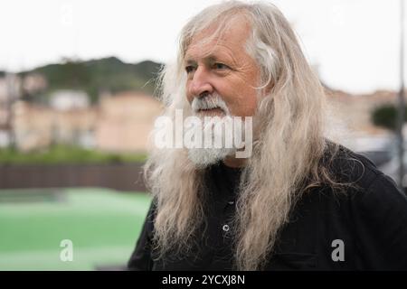 Elderly man with voluminous white hair stands outdoors, contemplating the idea of donating his hair, showcasing a thoughtful expression Stock Photo