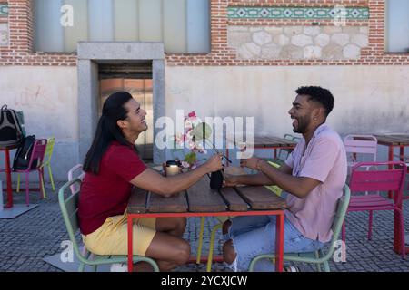 A moment of joy shared between a gay couple laughing together at an outdoor cafe table adorned with a pot of orchids The image shows a heartfelt expre Stock Photo