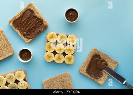 Overhead view of a breakfast setup with sliced whole-grain bread, chocolate spread, and banana slices neatly arranged on a cool blue background Perfec Stock Photo