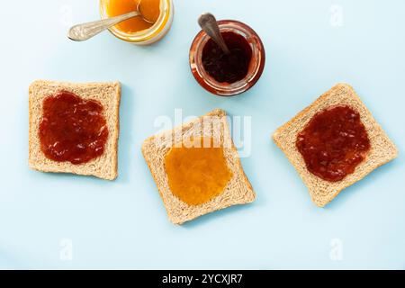An aerial view of toast slices topped with strawberry and peach jam alongside open jars Stock Photo