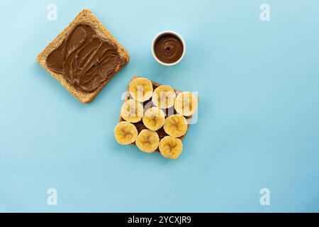 Wholewheat toast generously spread with chocolate and topped with neatly arranged banana slices on a solid pale blue background Stock Photo