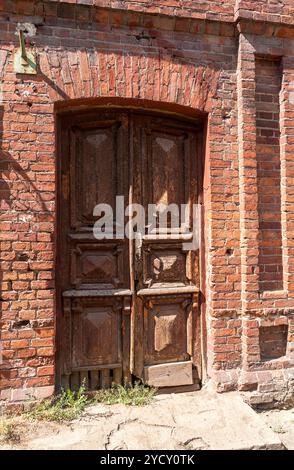 Old wooden door in the abandoned house from red bricks Stock Photo