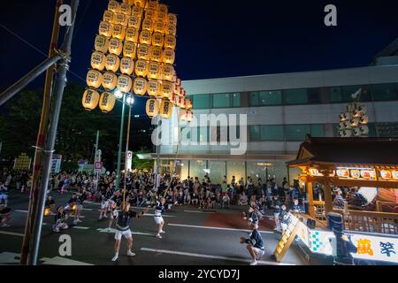 Akita, Japan - August 5, 2024: A group of young people in traditional costumes hold towering yellow lanterns during the lively Akita Kanto Festival. T Stock Photo