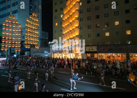 Akita City, Japan - August 5, 2024: Performers balance tall bamboo poles with multiple lanterns on various body parts, showcasing their skills at the Stock Photo