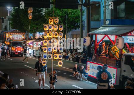 Akita, Japan - August 5, 2024: Young participants carry large Kanto lanterns through the streets of the city under the guidance of experienced elders. Stock Photo