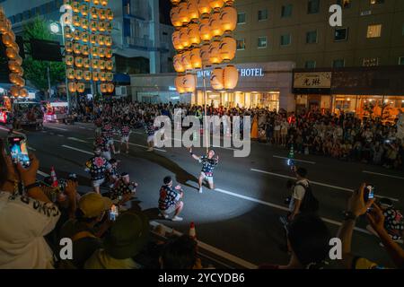 Akita City, Japan - August 5, 2024: Performers balance tall bamboo poles with multiple lanterns on various body parts, showcasing their skills at the Stock Photo