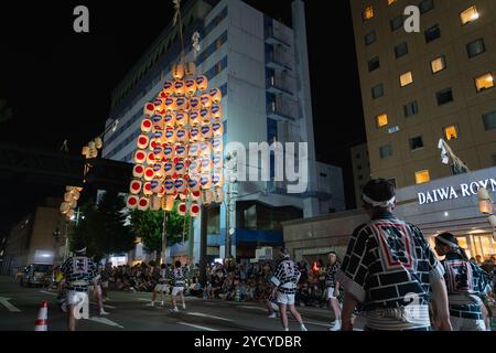 Akita City, Japan - August 5, 2024: Performers balance tall bamboo poles with multiple lanterns on various body parts, showcasing their skills at the Stock Photo