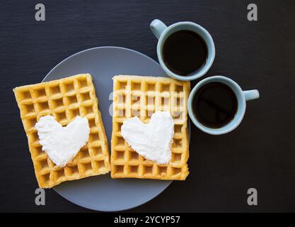 Delicious Belgian waffles with cream on a black background and two cups of coffee. Stock Photo