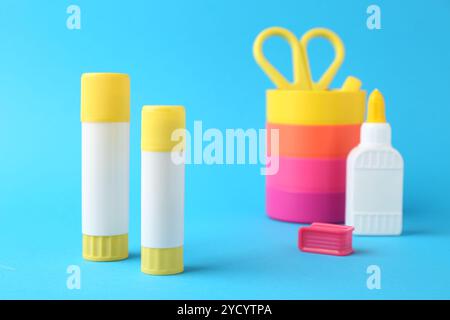 Different types of glue and colorful holder on light blue background, closeup Stock Photo