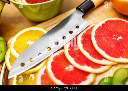 Sharp kitchen knife on cutting Board next to sliced grapefruit and other fruits Stock Photo