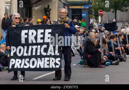 London, UK. 24th Oct 2024 The Free Political Prisoners public exhibition occupy Petty France outside the Ministry of Justice, directly challenging Attorney General Richard Hermer KC to engage with civil society, not just arms dealers and pop stars. The march to the Ministry of Justice where they sit in the road to protest. Hundreds of people have committed to take part in the action which will block the road to traffic in both directions for 90 minutes, or until the Attorney General agrees to a meeting. Protesters will hold up images of political prisoners, past and present, to the windows of Stock Photo