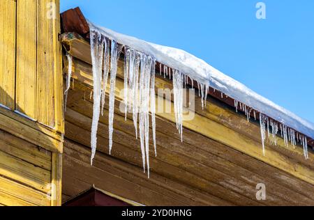 Transparent icicles on the roof of the wooden house Stock Photo