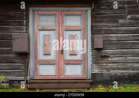 Painted front entrance of a wooden house. Wooden door background. Vintage pink and grey door on the exterior of old wooden house. Stock Photo
