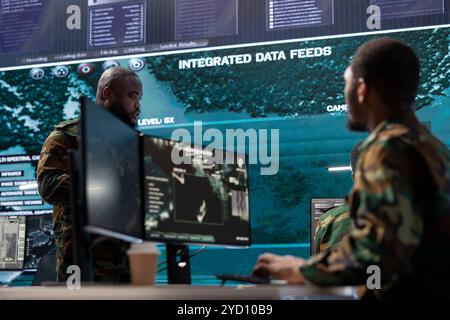 Cybersecurity team operates in an advanced military command center, managing surveillance systems and data protection. Army personnel work on national security operations using high tech gear. Stock Photo