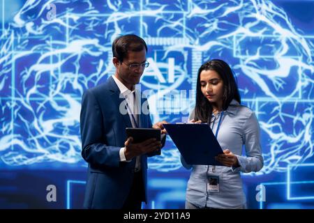 IT department coworkers solving tasks on laptop and tablet, running artificial intelligence programming scripts. Team of technicians brainstorming ways to develop AI applications Stock Photo