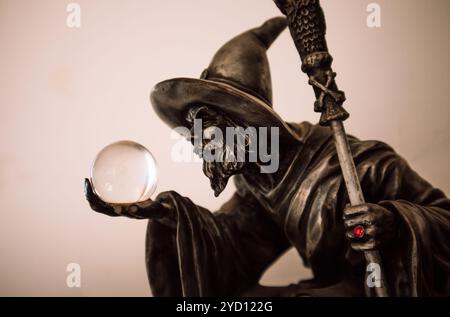 Dark wizard looking in a crystal magic ball in his hand. Fortune teller looks into the future. Halloween concept. Magician wearing a hat with red ring Stock Photo