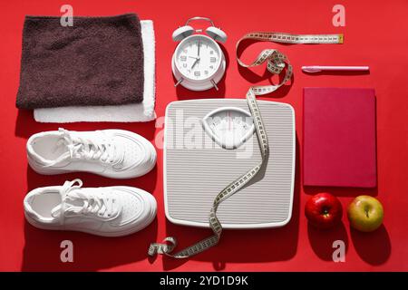 Scales with measuring tape, sneakers and alarm clock on red background. Weight loss concept Stock Photo
