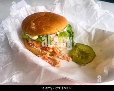 A lobster roll, dripping with mayonnaise and with a sliced pickle in a basket. At Young's Lobster Pound at the harbor of Belfast, Maine, USA. Stock Photo