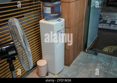 White water cooler with a blue lid. A fan is next to it. The fan is turned off Stock Photo