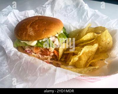 A lobster roll with kettle potato chips in a basket. At Young's Lobster Pound at the harbor of Belfast, Maine, USA. Stock Photo