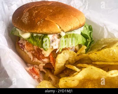 A lobster roll with kettle potato chips in a basket. At Young's Lobster Pound at the harbor of Belfast, Maine, USA. Stock Photo