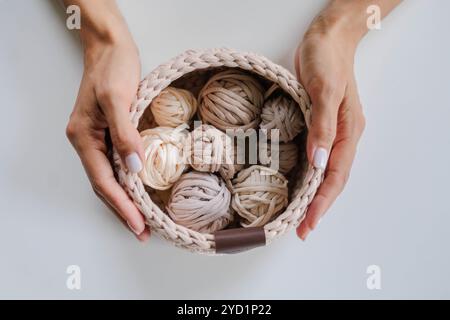 Female hands holding a crocheted basket with skeins of cotton yarn in natural tones and colors. Stock Photo