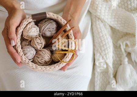 Female hands holding a crocheted basket with skeins of cotton yarn in natural tones Stock Photo