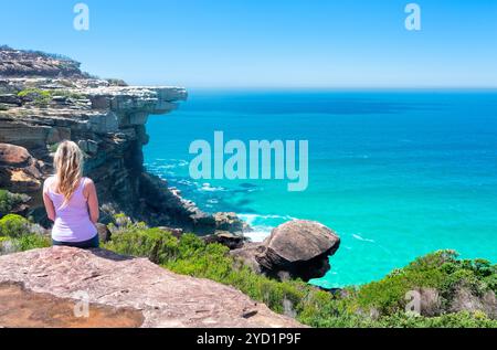 Female sitting on cliffs by the ocean Stock Photo