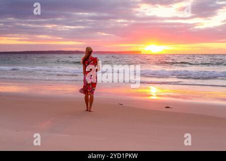 Woman standing on the wet sand of the beach watching sunrise Stock Photo