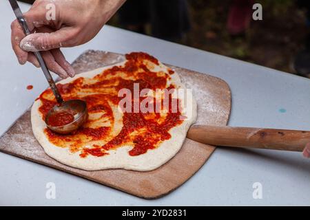 Man is spreading tomato paste on freshly kneaded pizza dough Stock Photo