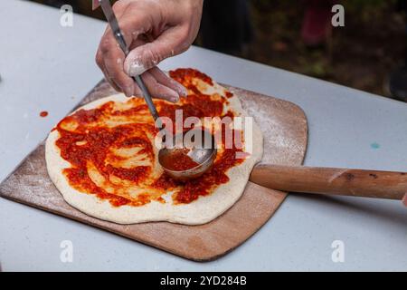 Man is spreading tomato paste on freshly kneaded pizza dough Stock Photo