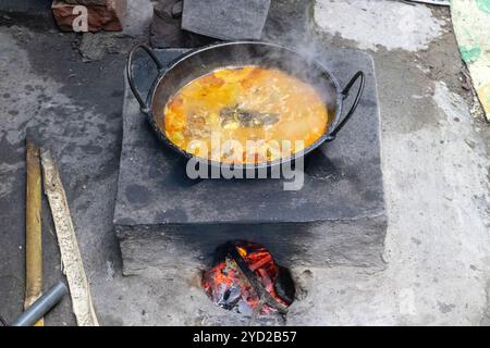 Rui fish curry is cooking on a traditional mud stove in a Bangladeshi village kitchen. This stoves made of clay and fueled with wood, commonly used by Stock Photo