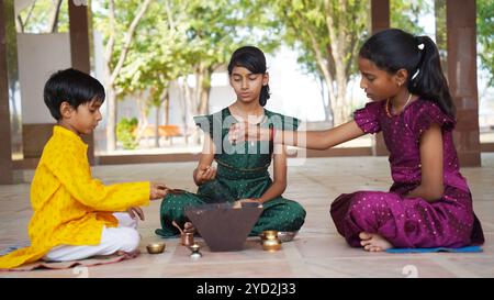 An Indian family in traditional attire performs a Yagya or Havan, led by a priest, to balance energies in their home. This sacred pooja is for harmony Stock Photo