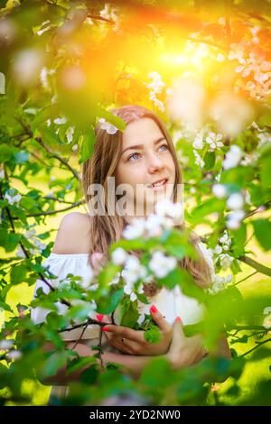 Portrait of a girl in a flowering Apple tree . A beautiful girl looks into the frame. Smile. Fair-haired girl. The flowering tree. Portrait spring Stock Photo