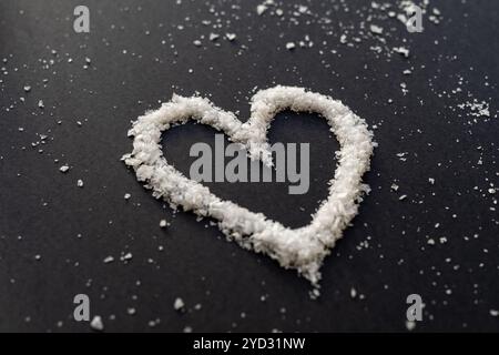 White flake salt shaped as a heart against black backround Stock Photo