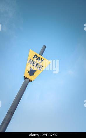 Conceptual Image Of A Bright Yellow Pay Here Sign Against A Blue Sky With Copy Space Stock Photo