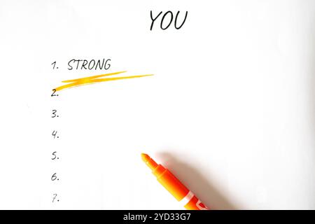 A marker is on a piece of paper with the word "strong" written in yellow. The paper is white and has a list of numbers on it Stock Photo