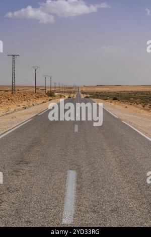 Vertical view of an endless desert highway and power lines leading through the rock and sand desert of southwestern Morocco Stock Photo