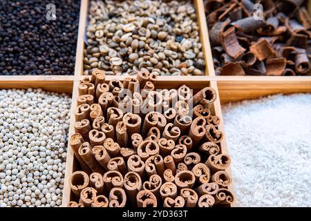 Various spices in wooden box. Cinnamon sticks, white pepper, coconut flakes, coffee beans and other seasonings top view, selective focus. Stock Photo