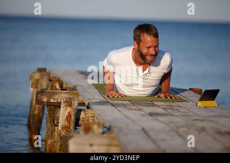 Happy man, lake and yoga with tablet for online tutorial, lesson or virtual class in nature. Mature, male person or yogi with smile for holistic Stock Photo