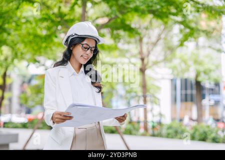 Portrait smart young engineer women standing with floorplan at green park nature. Environmental saving energy project designer. Stock Photo