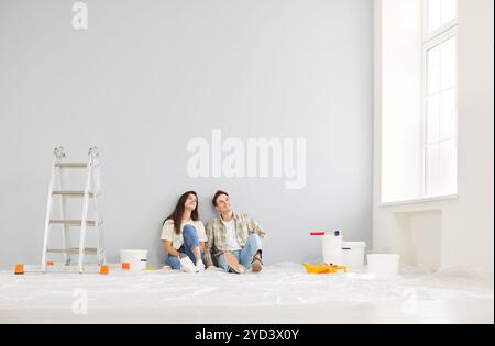 Young relaxed family couple sitting on the floor, planning home repair in their house or apartment. Stock Photo